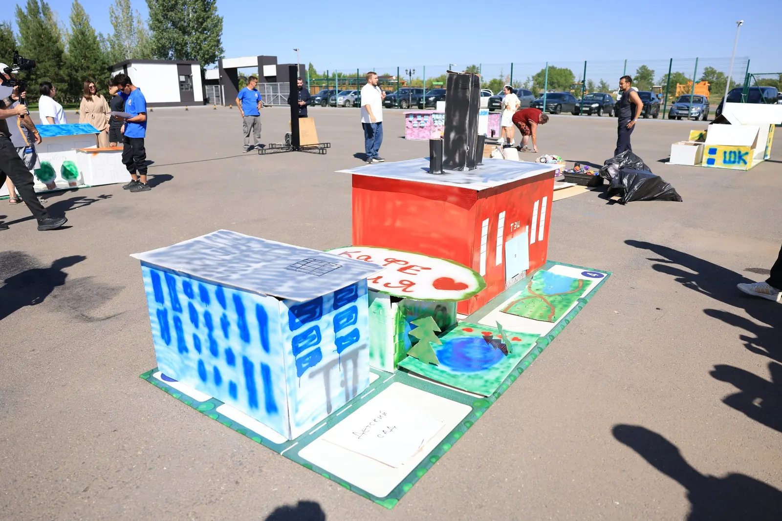 Сектор города из гофрокартона, собранный командой на тимбилдинге New Urban Code в Астане: синий жилой дом, красная ТЭЦ с трубами, кафе и парк с прудом